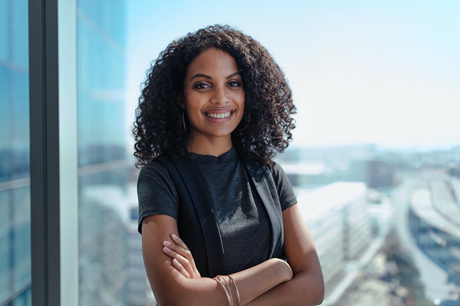 Contact Us - Businesswoman Standing in Front of a Window in a High Rise Building, Arms Folded and Smiling