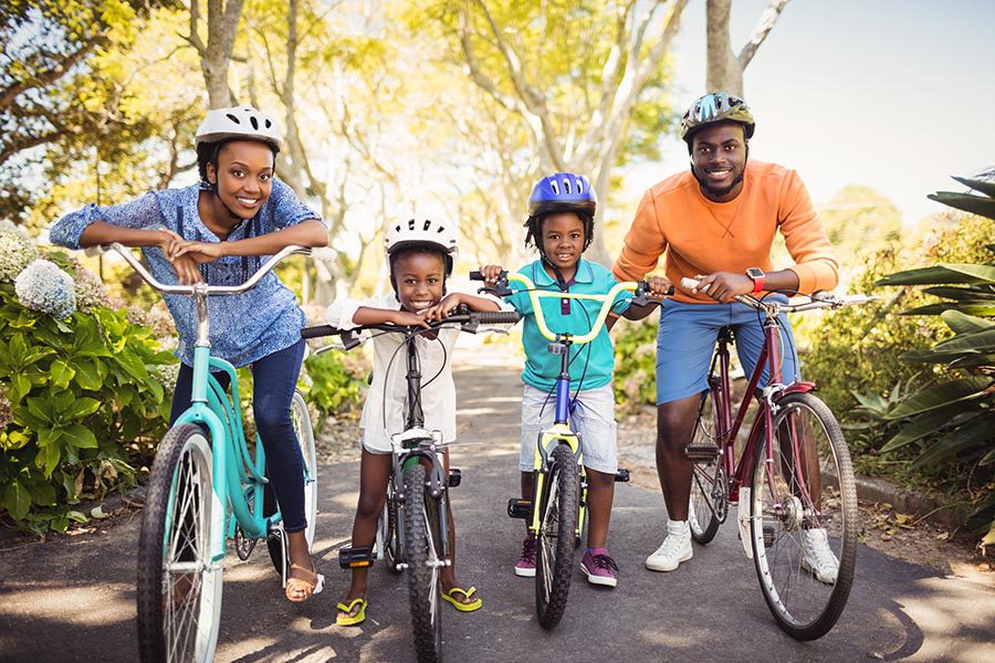 Personal Insurance - Family of Four Pauses on a Bike Ride in a Green Park, Everyone Smiling and Wearing Brightly Colored Clothing and Helmets