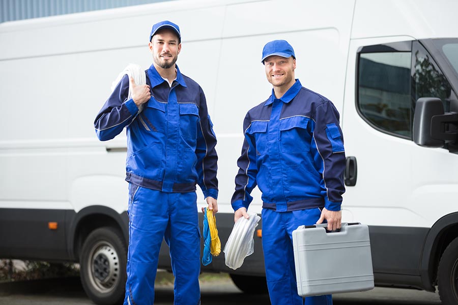Specialized Business Insurance - Two Contractors Stand in Front of Their White Service Van, Wearing Blue Coveralls and Holding Tools